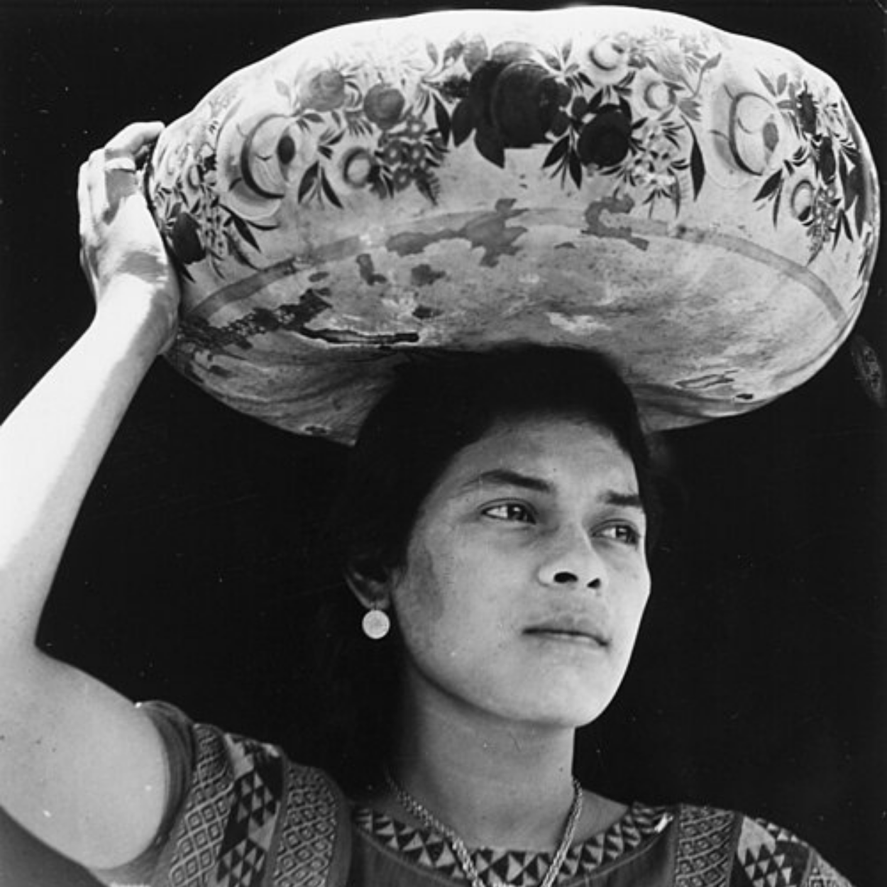 Black and white photograph of a woman carrying a painted bowl