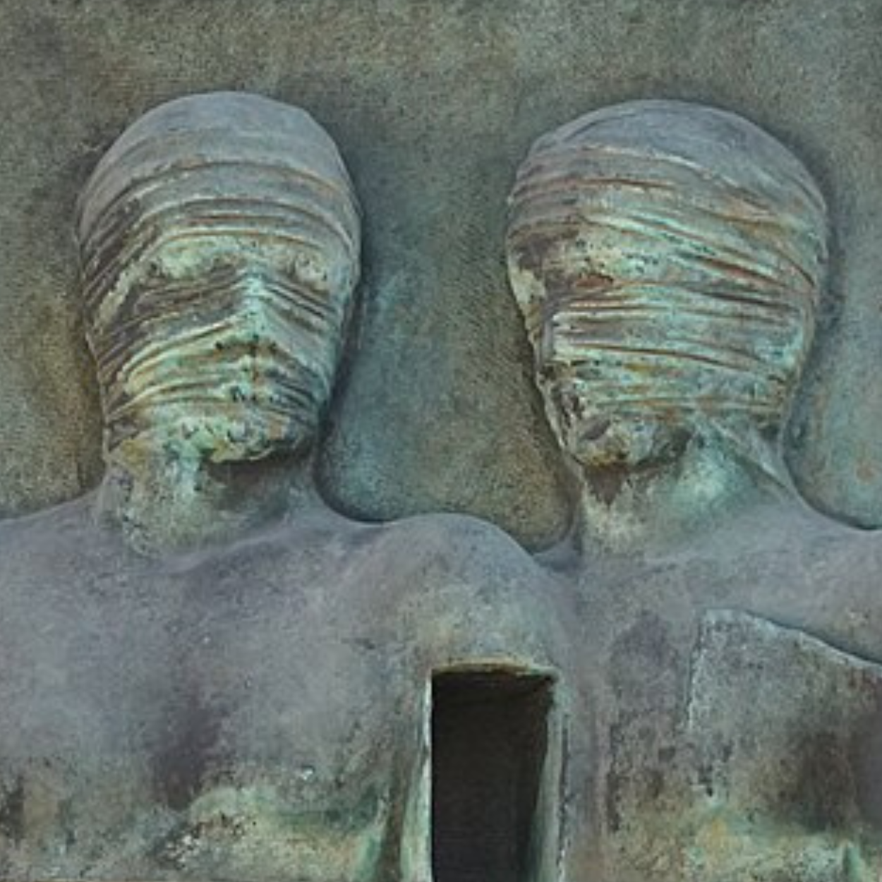 Weathered bronze relief of two figures with wrapped faces